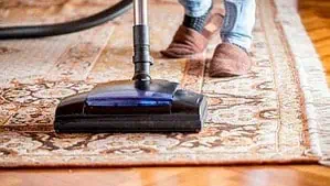 Man is vacuuming a rug using upright vacuum
