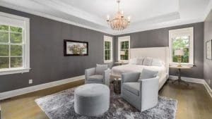 Bedroom with gray walls and white ceiling and white bed set furnished with furniture and shag rug.