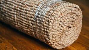 A rolled sisal carpet in earth tone and brown color is palaced on a brown hardwood floor.