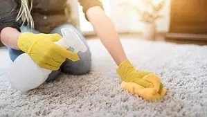 A woman is spot cleaning a white color push carpet wearing yellow gloves