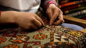 Repair man is repairing a rug with special needle and wool