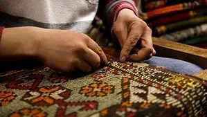 Repairman is repairing a rug with special needle and wool