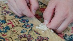 Repair man is in process of repairing the edge of a Persian Kerman rug
