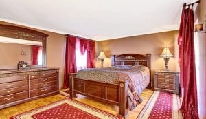 A colorful bedroom with red drapery and red colors on the brown color hardwood floor.