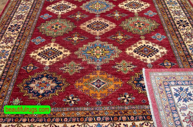 Hand knotted oriental carpet with red color in center and beige in borders, the design is Kazak.