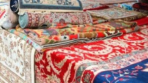 Several rugs in many colors rolled and laid on a bench.