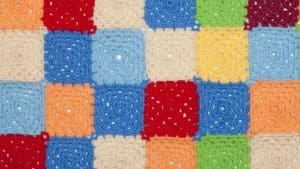 Sample of a multicolor hooked rug with squares on red, beige, green, yellow and orange colors.