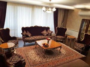 A living room with a beige Persian rug on floor, coffee table and furniture in burgundy and gold colors.