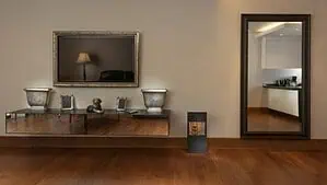 A room with a brown hardwood floor, a tall mirror and picture frame on the wall A room with a brown hardwood floor, a tall mirror and picture frame on the wall