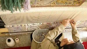 Woman is sitting in front of a loom and weaving Persian rug while she is looking at the rug map to choose the right colors. Woman is sitting in front of a loom and weaving Persian rug while she is looking at the rug map to choose the right colors.