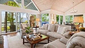 Image of a living room with a white rug and white furniture on the hardwood floor, glass windows, coffee table and lamps. Image of a living room with a white rug and white furniture on the hardwood floor, glass windows, coffee table and lamps.