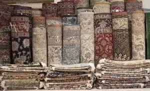 Some rugs are rolled up with ropes and some rugs are folded and stacked on top of each other.